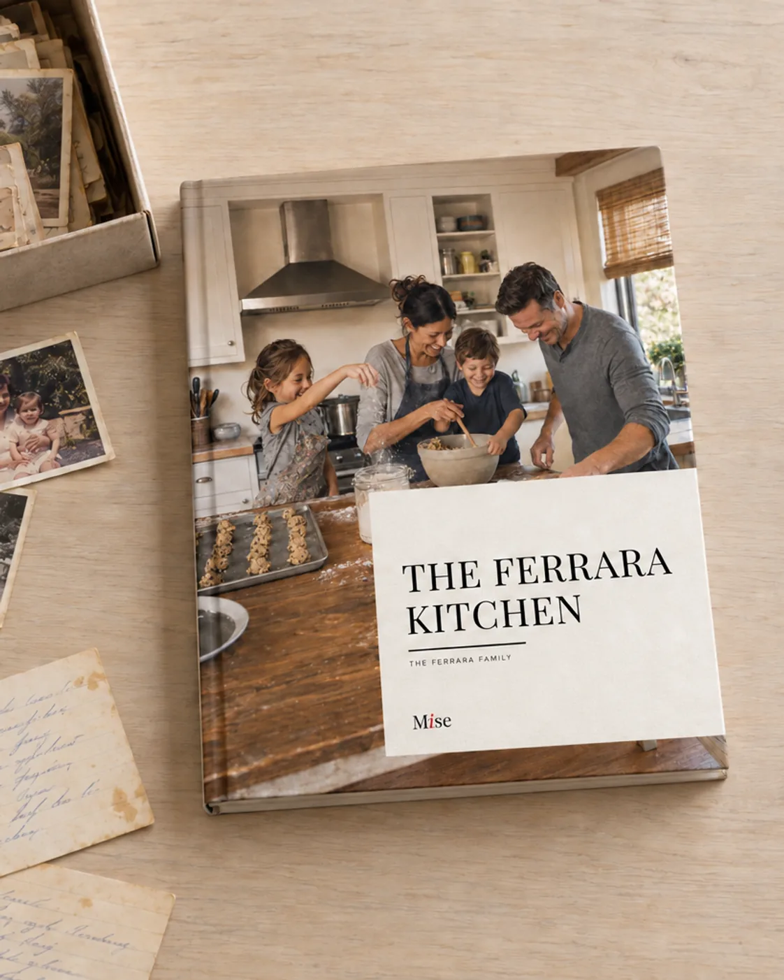 A finished Mise hardcover, The Ferrara Kitchen, on a table beside a shoebox of handwritten family recipe cards and old photographs